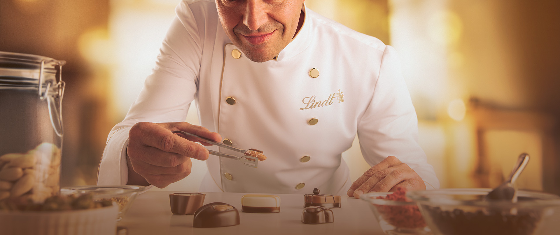 Maître chocolatier Urs Liechti dekoriert Pralinen und hält eine Mandel in einer Zange. (Foto)